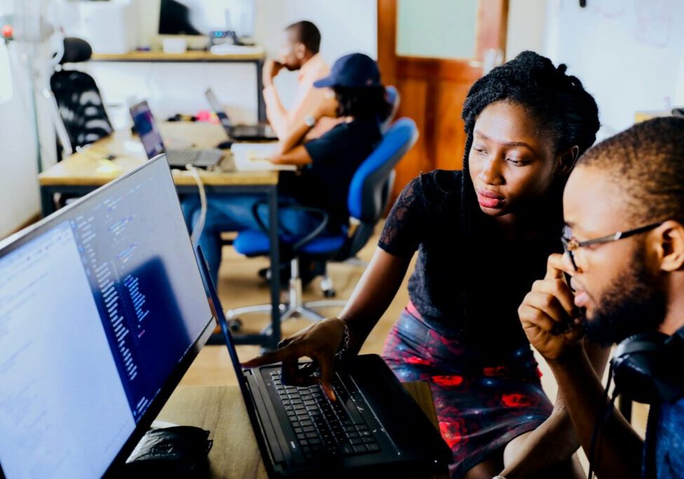 Two students looking at a two computer monitors.